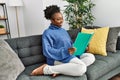 African american woman reading book sitting on sofa at home Royalty Free Stock Photo