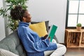 African american woman reading book sitting on sofa at home Royalty Free Stock Photo