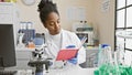 African american woman scientist reading notes in a laboratory setting with a microscope and glassware Royalty Free Stock Photo