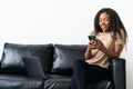 African American woman sit relax on couch at home use modern cellphone text message online. Happy young ethnic female rest on sofa Royalty Free Stock Photo