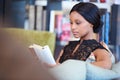 African American woman sitting comfortably on sofa while reading book