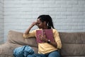 African American woman sitting at cozy apartment at home reading a book and she is sad and crying because what she read. Novel Royalty Free Stock Photo