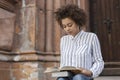 African-American woman sitting on the street and reading a book. On legs books. There`s a building next to a dark-skinned girl Royalty Free Stock Photo