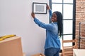 African american woman smiling confident hanging photo on wall at new home Royalty Free Stock Photo