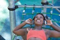 African American woman in sports clothes and white headphones, lying down and smiling, listening to music in a playground. Concept Royalty Free Stock Photo