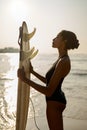African american woman standing in front of surfboard on ocean beach. Black female surfer looking at surf board. Pretty Royalty Free Stock Photo