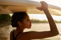 African american woman standing with surfboard on her head on ocean beach. Black female surfer posing with surf board Royalty Free Stock Photo