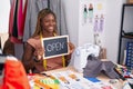 African american woman tailor sitting on table holding open blackboard message at tailor shop