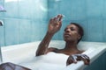 African American woman, taking a bath with the bathtub full of foam and playing with soap bubbles. Concept bath, relax, foam, soap
