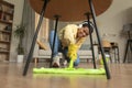 African american woman trying to mop floor under table, cleaning living room and listening to music in headphones Royalty Free Stock Photo