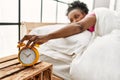 African american woman turning off alarm clock lying on bed at bedroom Royalty Free Stock Photo