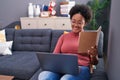 African american woman using laptop reading book at home Royalty Free Stock Photo