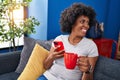 African american woman using smartphone drinking coffee at home Royalty Free Stock Photo