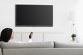 African american woman watching TV pointing remote control at flatscreen plasma television set with blank screen, mockup