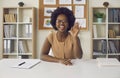 African american woman waving hand looking at camera sitting at office desk Royalty Free Stock Photo