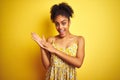 African american woman wearing casual floral dress standing over isolated yellow background clapping and applauding happy and