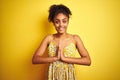 African american woman wearing casual floral dress standing over isolated yellow background praying with hands together asking for