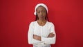 African american woman wearing christmas hat standing with serious expression and arms crossed gesture over isolated red Royalty Free Stock Photo