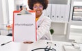 African american woman wearing doctor uniform holding clipboard with hypothyroidism message at clinic Royalty Free Stock Photo