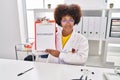 African american woman wearing doctor uniform holding clipboard with hypothyroidism message at clinic Royalty Free Stock Photo