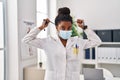 African american woman wearing doctor uniform and medical mask holding stethoscope at clinic Royalty Free Stock Photo