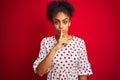 African american woman wearing fashion white dress standing over isolated red background asking to be quiet with finger on lips Royalty Free Stock Photo