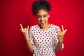 African american woman wearing fashion white dress standing over isolated red background shouting with crazy expression doing rock Royalty Free Stock Photo