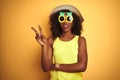 African american woman wearing funny pineapple sunglasses over isolated yellow background smiling with happy face winking at the Royalty Free Stock Photo