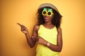 African american woman wearing funny pineapple sunglasses over isolated yellow background smiling and looking at the camera Royalty Free Stock Photo