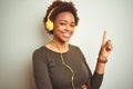 African american woman wearing headphones listening to music over isolated background with a big smile on face, pointing with hand Royalty Free Stock Photo