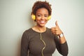 African american woman wearing headphones listening to music over isolated background doing happy thumbs up gesture with hand Royalty Free Stock Photo