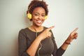 African american woman wearing headphones listening to music over isolated background smiling and looking at the camera pointing Royalty Free Stock Photo