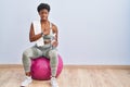 African american woman wearing sportswear sitting on pilates ball pointing aside worried and nervous with forefinger, concerned Royalty Free Stock Photo