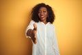 African american woman wearing striped shirt standing over isolated yellow background smiling friendly offering handshake as