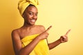 African american woman wearing towel after shower standing over isolated yellow background smiling and looking at the camera Royalty Free Stock Photo