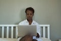 African American woman in a white shirt and sitting on the bed, working with her laptop. Concept teleworking, internet, working Royalty Free Stock Photo