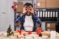 African american woman working at small business doing christmas decoration doing ok gesture like binoculars sticking tongue out,