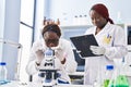 African american women scientists using microscope writing on document at laboratory Royalty Free Stock Photo