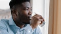 African american young dreaming man thoughtful positive guy turn head look at window drink fresh cold water glass of Royalty Free Stock Photo