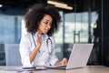 African american young female doctor sitting in clinic office at table and talking online with patient, consulting and Royalty Free Stock Photo