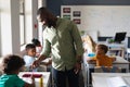 African american young male teacher assisting elementary boy studying at desk in classroom Royalty Free Stock Photo