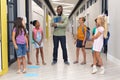 African american young male teacher talking to multiracial elementary students standing in corridor