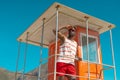 African american young man wearing sunglasses shielding eyes on lifeguard hut at beach against sky Royalty Free Stock Photo