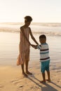 African american young woman holding son\'s hands while standing on beach against clear sky at sunset Royalty Free Stock Photo