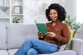 African American young woman relaxing at home, sitting on the sofa and reading a book Royalty Free Stock Photo