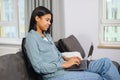 African-american young woman spending home leisure with laptop. Calm mixed-race girl sitting at cozy sofa and looking at