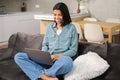 African-american young woman spending home leisure with a laptop. Smiling mixed-race girl sitting at the cozy sofa and