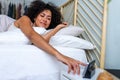 African American young woman waking up happy after good night sleep reaching hand to turn off alarm clock. Royalty Free Stock Photo