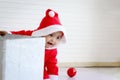 African baby kid in Santa Claus red costume hiding behind big gift box present in white living room, beautiful little child Royalty Free Stock Photo