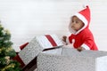 African baby kid in Santa Claus red costume stands near big gift box present at white room, beautiful little child celebrates